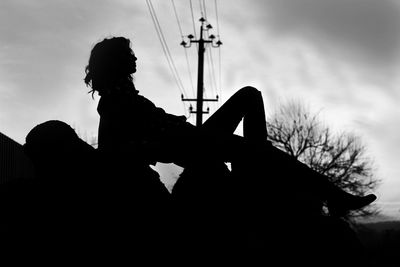 Low angle view of silhouette man sitting against sky