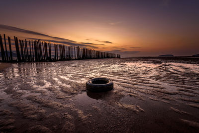 Tire on sand against sky during sunset