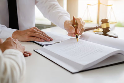 Midsection of judge writing on table while colleague sitting