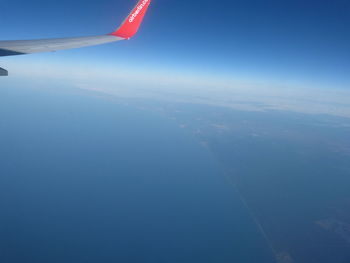 Aerial view of airplane wing over landscape against blue sky