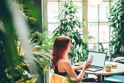 Woman using mobile phone and laptop during rest in coffee shop.