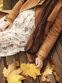 Low section of woman holding autumn leaves on wood