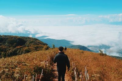 Rear view of man walking on mountain against sky