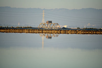 Electricity pylon by lake against sky