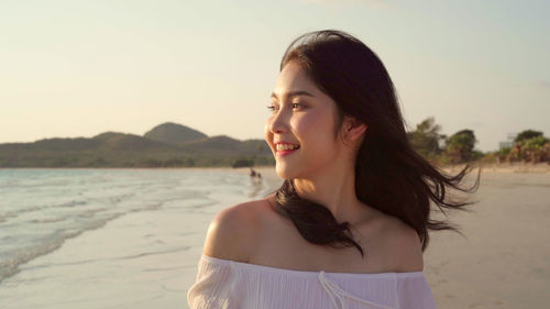 Portrait of smiling young woman on beach against sky