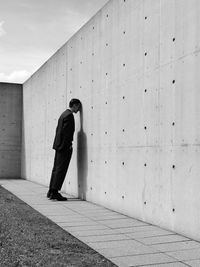 Full length of depressed man standing by wall