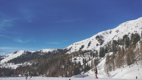 Man skiing on snow covered field against blue sky