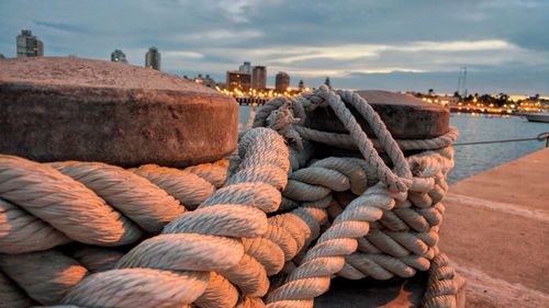 Close-up of rope tied to bollard at harbor against sky