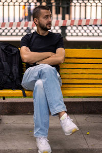 Thoughtful caucasian man sits on a yellow bench in a square. outdoor male portrait