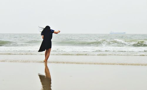 Full length rear view of woman walking at beach against clear sky