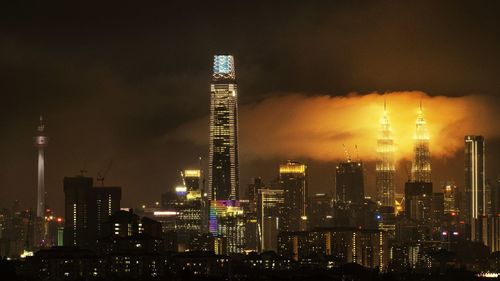 Illuminated modern buildings in city against sky at night