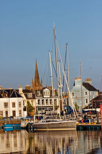 Sailboats moored on harbor by buildings against clear sky