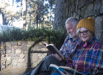 Senior man and woman reading book while sitting by wall