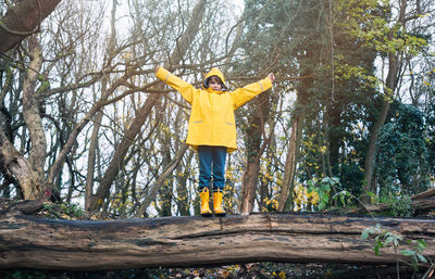 Full length of boy with arms outstretched wearing raincoat and rubber boots on tree