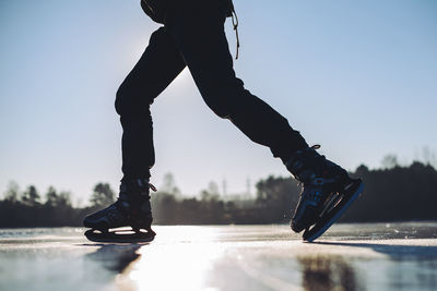 Low section of man ice-skating against clear sky