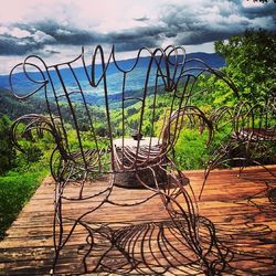 Empty bench against cloudy sky