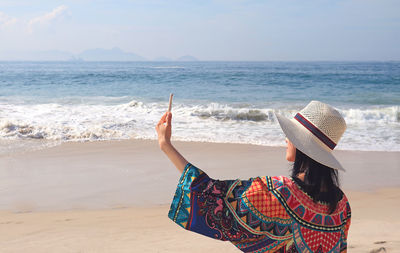 Rear view of woman taking selfie at beach