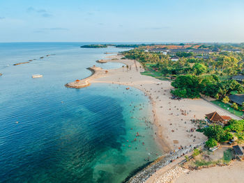 Aerial drone view of holiday in sanur beach, bali, indonesia with ocean, boats, beach, and people.