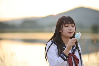 Portrait of young woman drinking water against lake