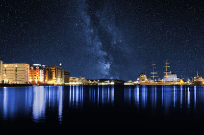 Illuminated buildings by sea against sky at night