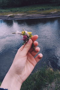 Cropped hand of woman holding flowers against lake