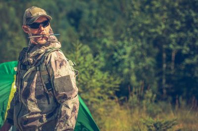 Army solider wearing sunglasses while standing against trees in forest