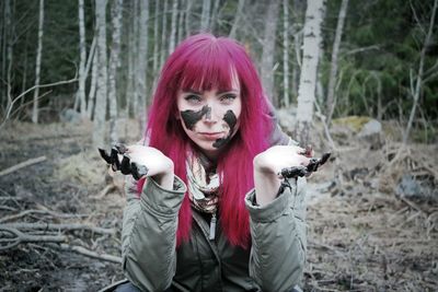 Portrait of redhead woman with mud on face crouching in forest