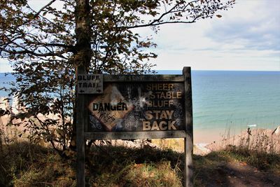 Information sign on tree by sea against sky