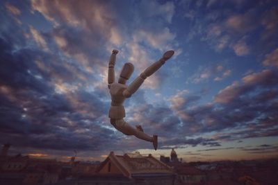 Wooden figurine in mid-air against cloudy sky during sunset