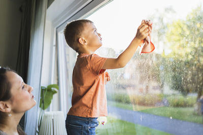 Son helping mother to clean window at home