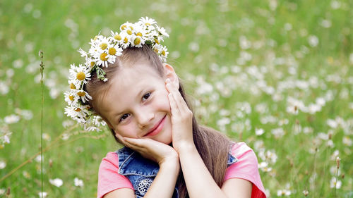 On a chamomile lawn, a sweet girl in a wreath of daisies, smiling, pressing her hands to her cheeks