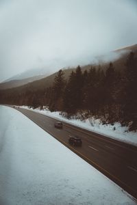 Road by trees against sky during winter