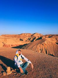 Mid adult man sitting on mountain against blue sky during sunny day