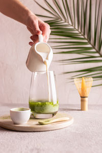 Woman pouring milk into a glass with green tea matcha