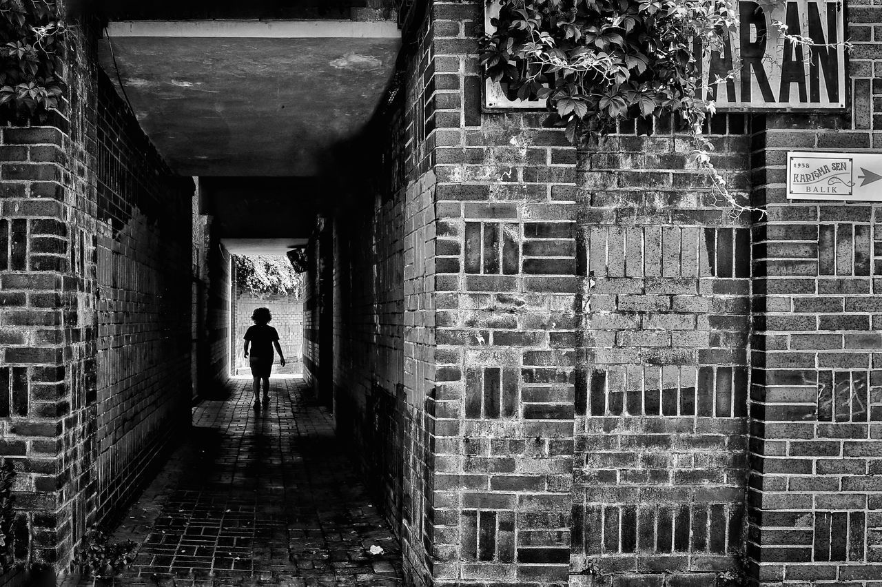 REAR VIEW OF MAN STANDING ON ALLEY