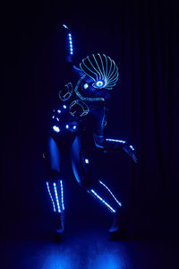 Faceless person in contemporary glowing suit of space cyborg with neon illumination and helmet standing on black background in dark studio person