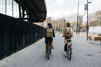 Rear view of couple riding e-bikes in the city talking to each other