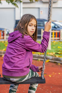 Portrait of girl sitting on swing at playground