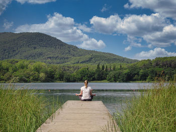 Rear view of woman sitting on bench against mountain