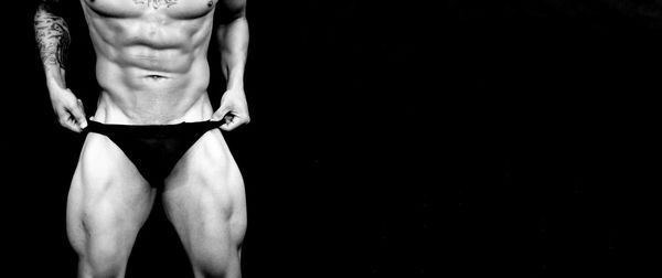 Midsection of muscular man standing against black background