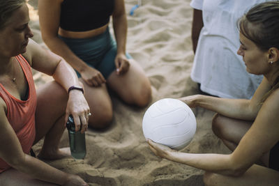High angle view of woman holding volleyball with friends kneeling on sand