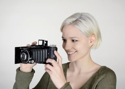 Portrait of smiling woman holding camera against white background