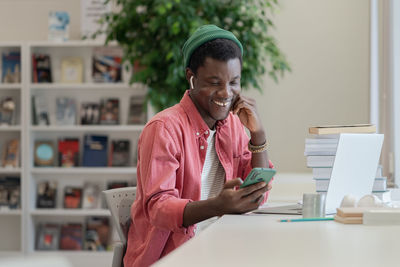 Happy african american student guy using mobile device while studying in library