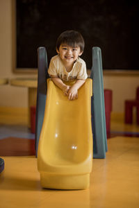 Portrait of smiling boy leaning on slide at classroom