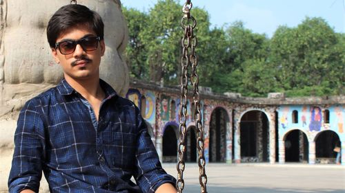 Portrait of young man wearing sunglasses sitting on swing