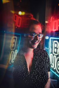 Portrait of smiling young woman in sunglasses at night