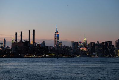 East river by illuminated empire state building in city against sky during sunset