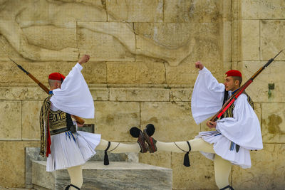 Rear view of men holding umbrella against wall