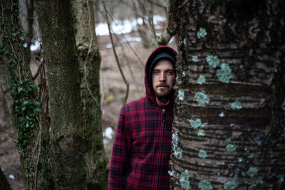Portrait of young man standing by tree trunk in forest