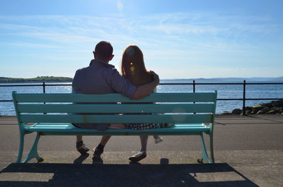 Rear view of couple sitting bench against sea